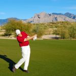Golfer hitting a golf ball at the OMNI Tucson National Golf Course in Tucson, Arizona with mountains behind