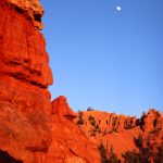 red rocks rising with the moon in the distance